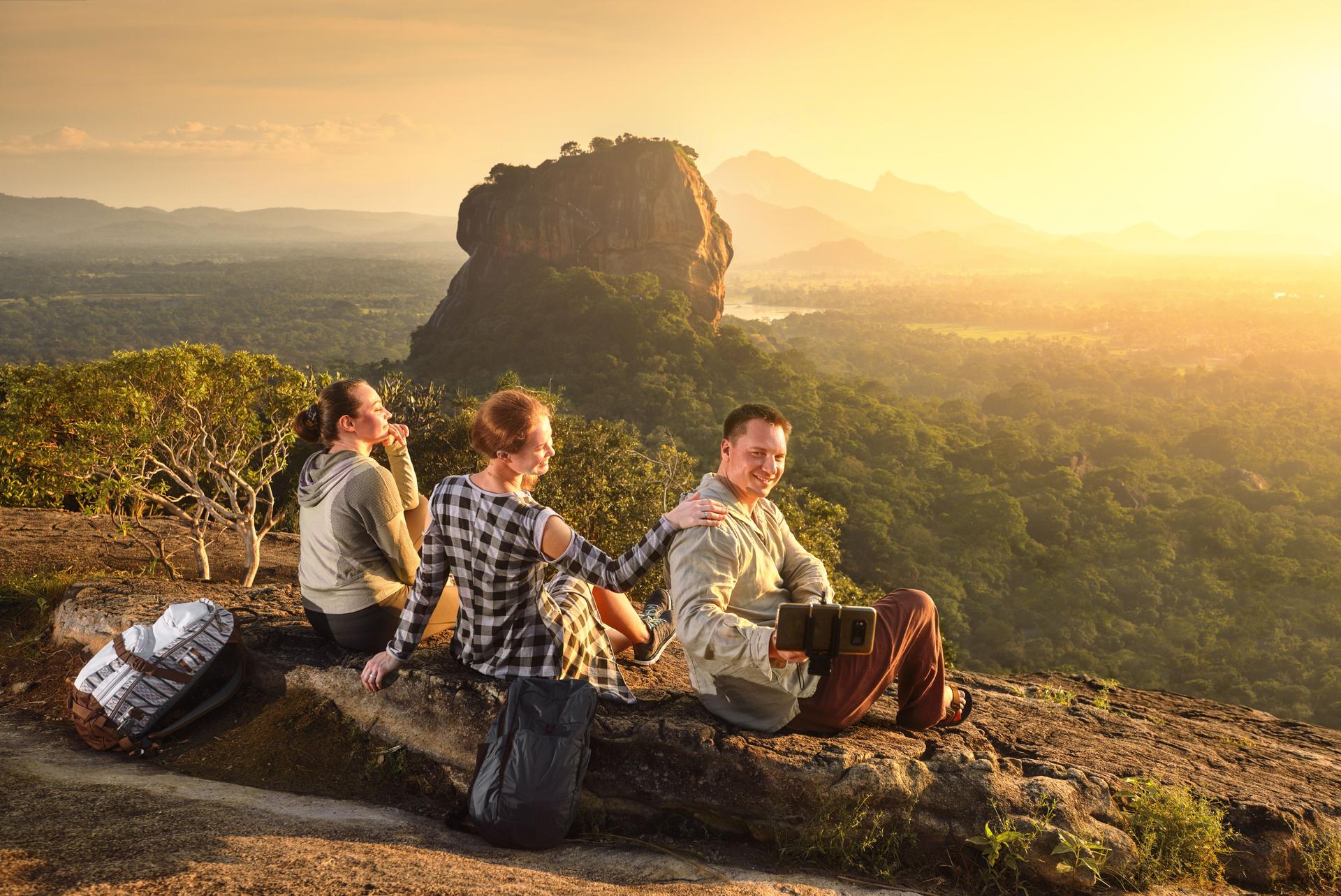 Three young tourists relaxes and watches during vacation colorful sunset on background of famous rocky plateau Lion peak, Sigiriya. Sri Lanka