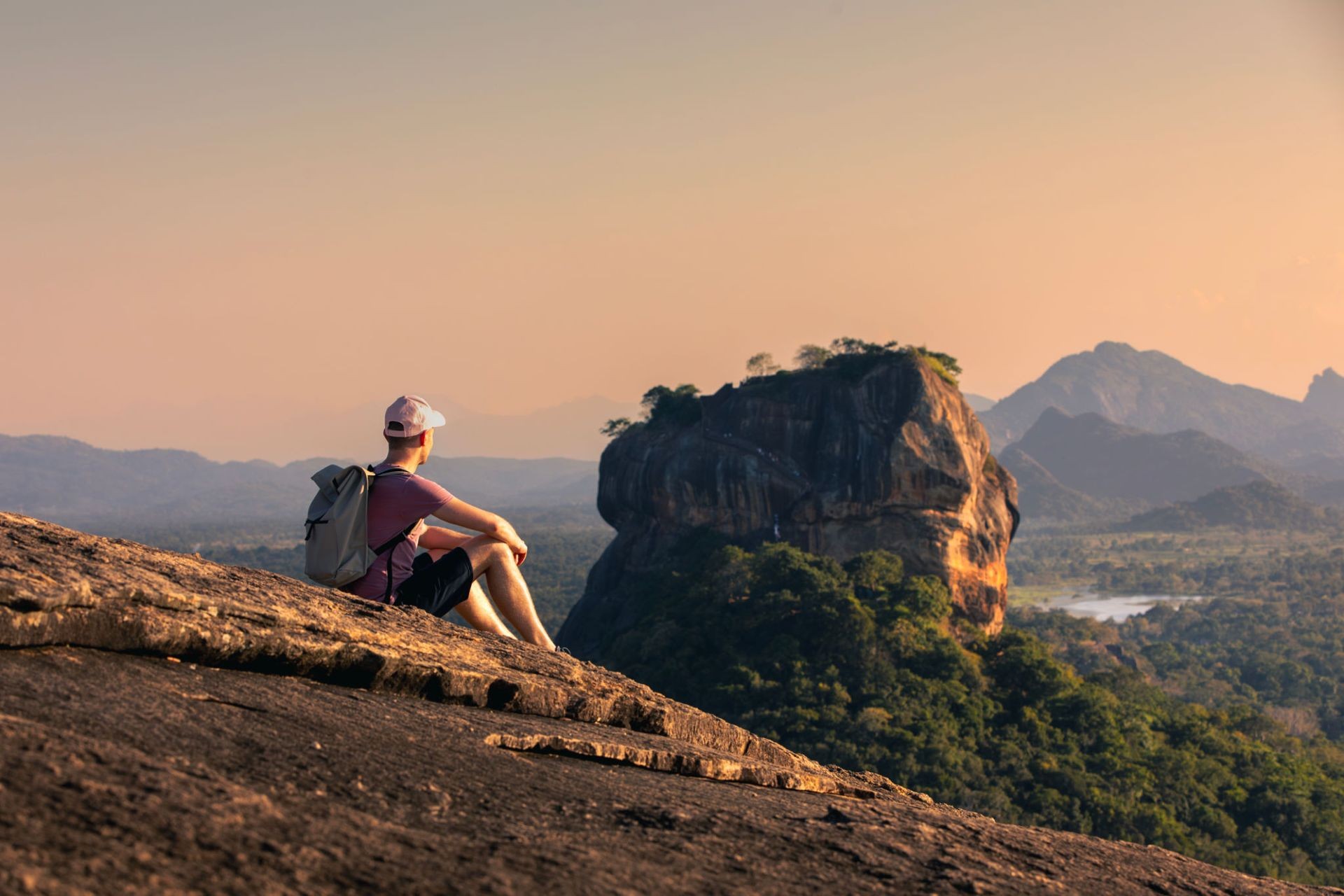 Man with backpack sitting on rock and looking at landscape.