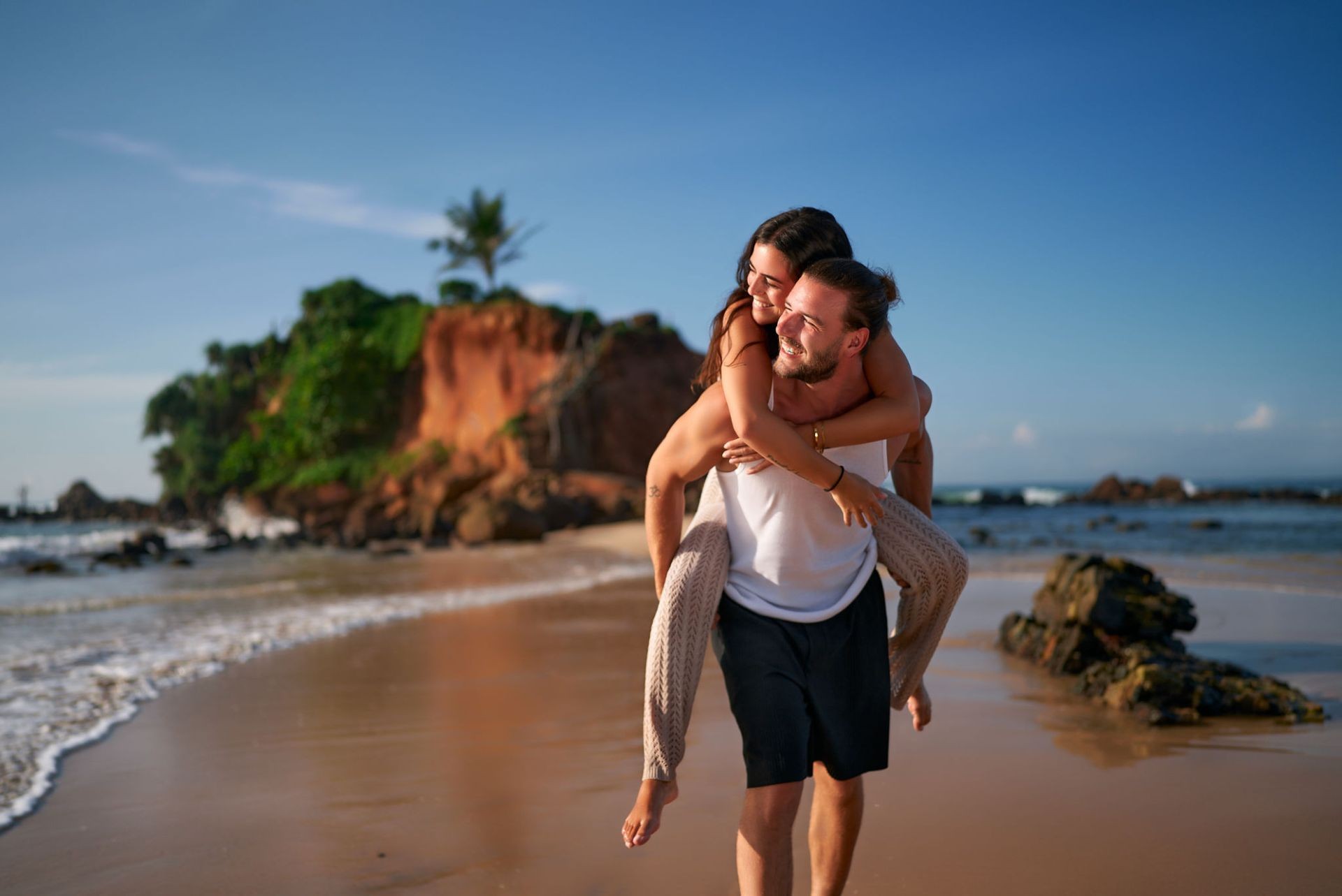 Man carrying a woman on his back on a sunny beach, smiling and enjoying the moment.